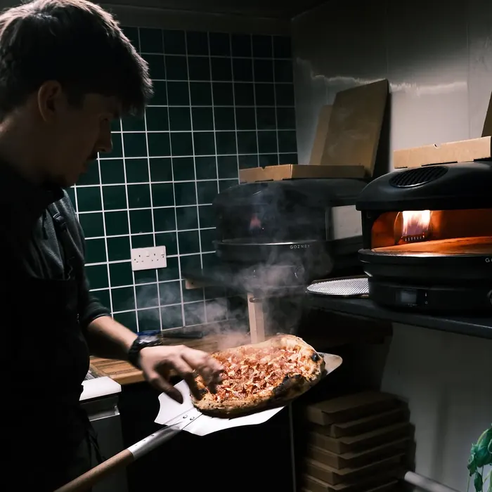 A wood-fired pizza going into the oven on a peel.